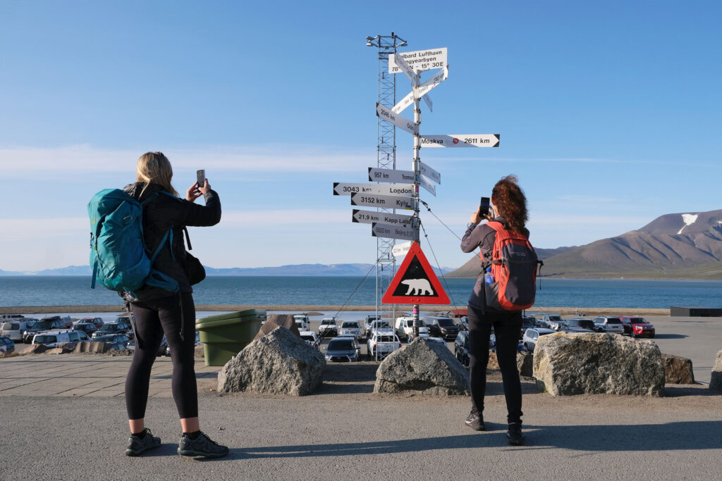 two people standing by a distance sign in svalbard to show the language of Svalbard
