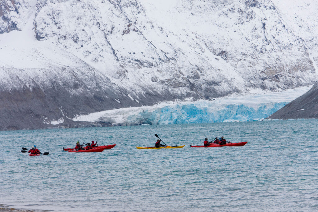 A group of sea kayakers in Svalbard with a glacier in the background